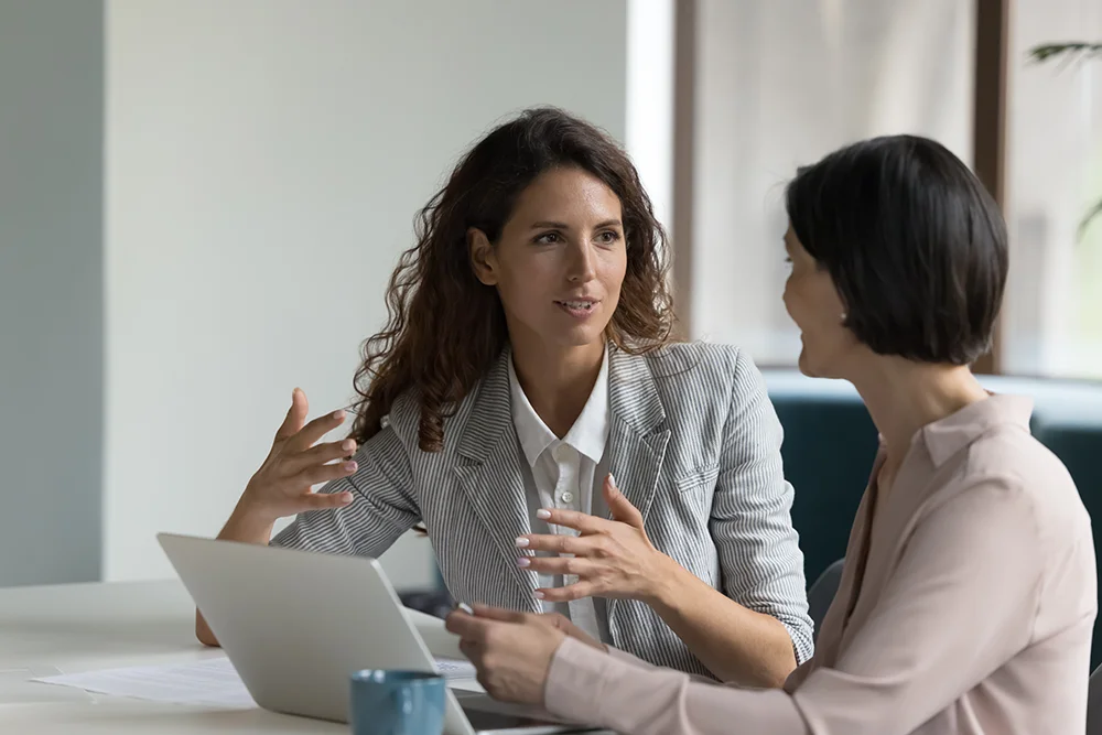 Zwei Geschäftsfrauen sitzen am Tisch und führen ein Gespräch im Büro.