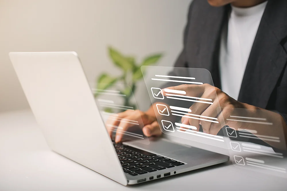 Büroarbeit mit Laptop, Formularen und Brille auf dem Tisch.